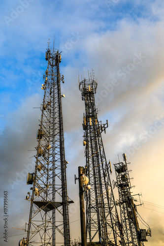 Low angle view of telecommunications towers against cloudy sky
