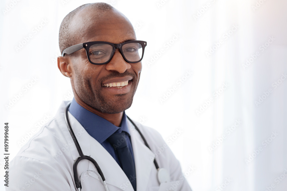 Help people. Gay afro american male doctor posing on light background while smiling and gazing at camera Help people. Gay afro american male doctor posing on light background while smiling and gazing at camera