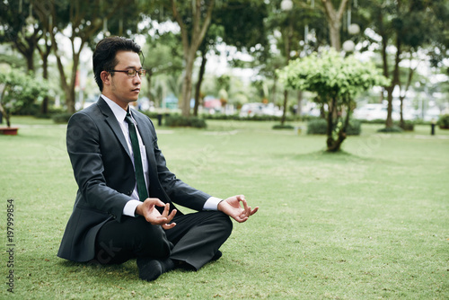 Young Asian businessman in suit practicing outdoor meditation in park © DragonImages