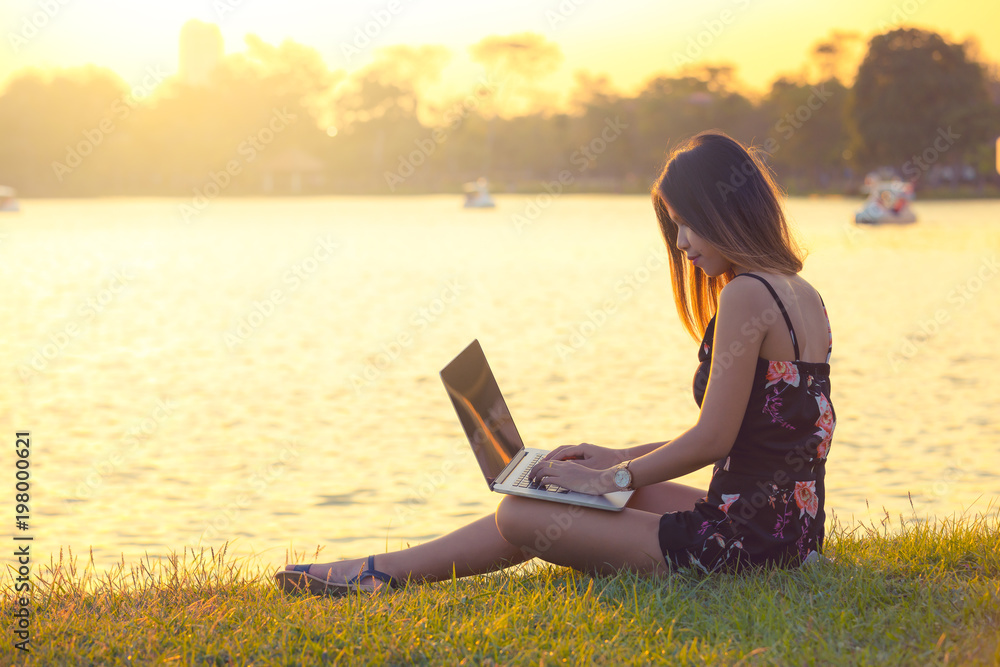 attractive women using laptop in park during sunset . Thailand , Southeast Asia