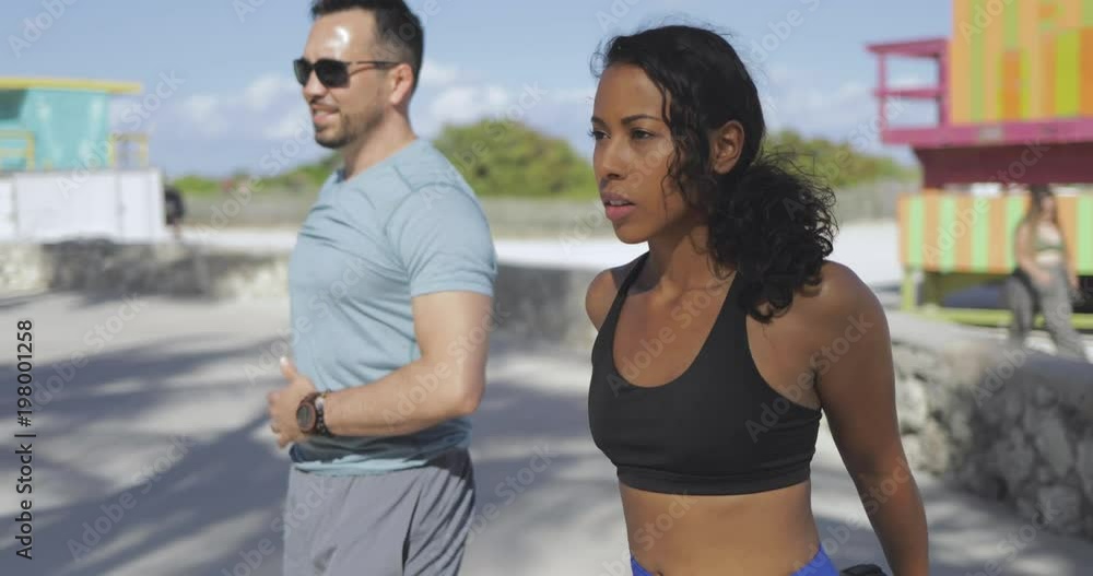 Concentrated sportive black woman with man stretching and working out in sunlight looking forward on waterfront. Concentrated sportive black woman with man stretching and working out in sunlight looking forward on waterfront.