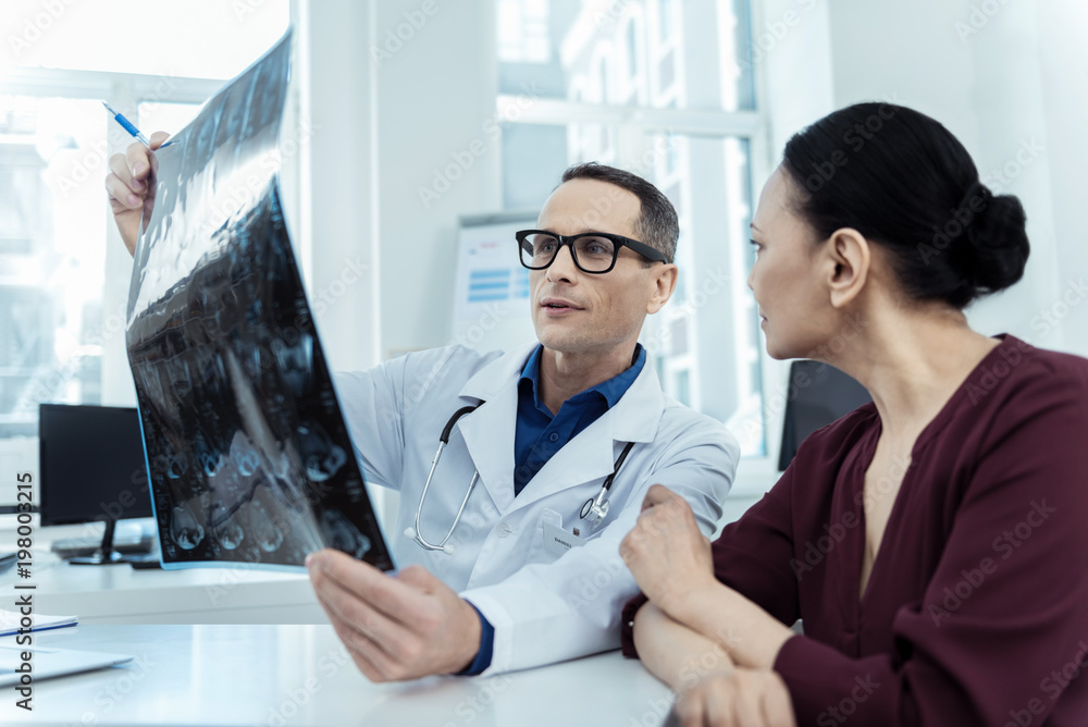 Involved in work. Pleasant male neurologist sitting at the table with his patient Involved in work. Pleasant male neurologist sitting at the table with his patient