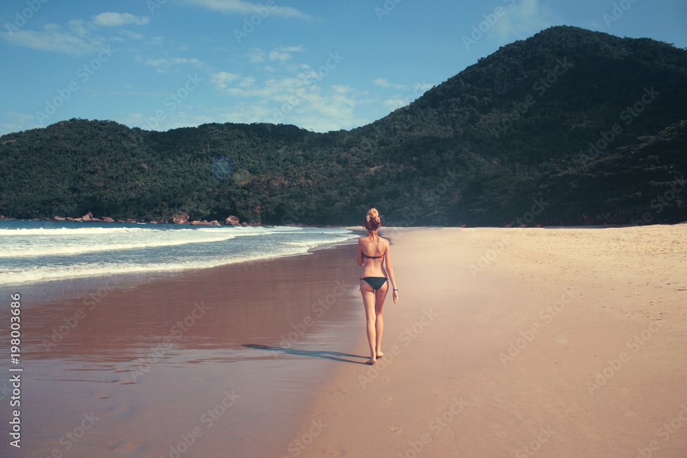 young woman in swimsuit walking along the seashore, Brazil