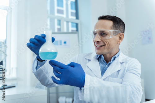 Waiting for result. Cheerful professional scientist holding a flask while working in a lab