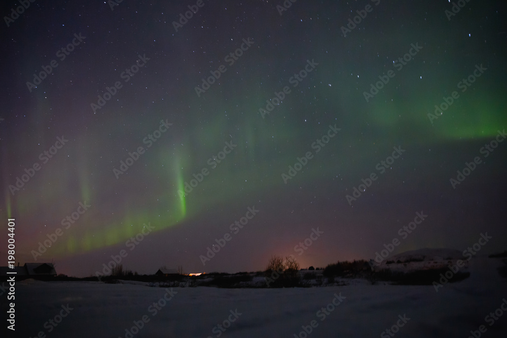 village with houses under sky with majestic aurora borealis in iceland