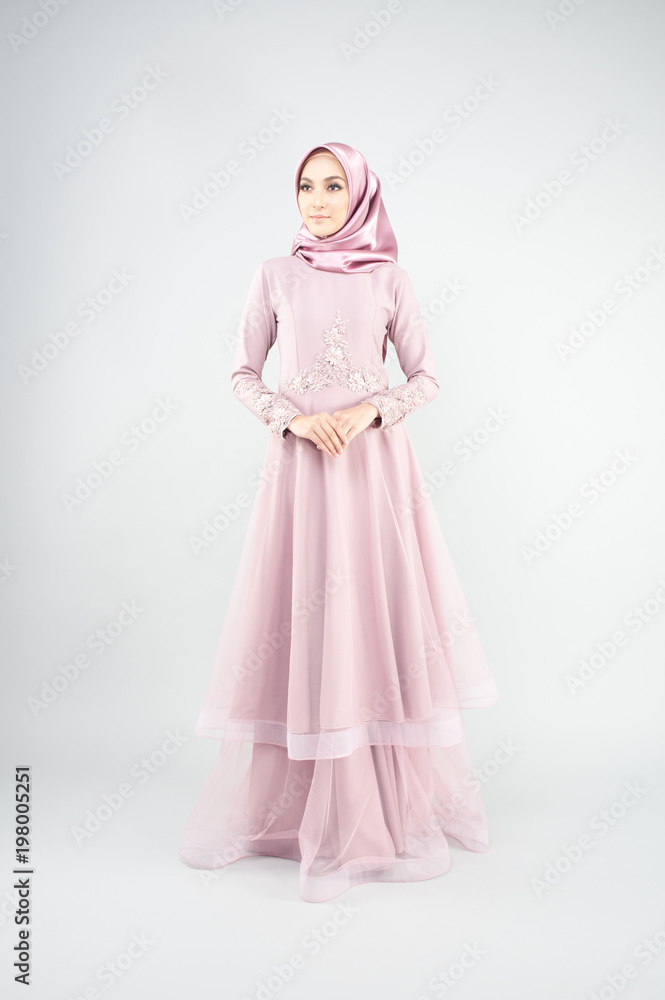 Attractive young Muslim girl wearing pink dress and hijab with grey background.Hijab Fashion Portraiture.
