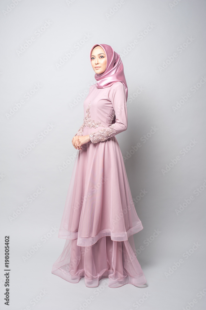 Attractive young Muslim girl wearing pink dress and hijab with grey background.Hijab Fashion Portraiture. Stock Adobe Stock