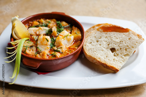 Fish soup with cod. Appetizing Spanish dish All i pebre in a clay plate with lemon and a slice of bread. Potatoes with fresh fish meat in a fragrant garlic sauce.