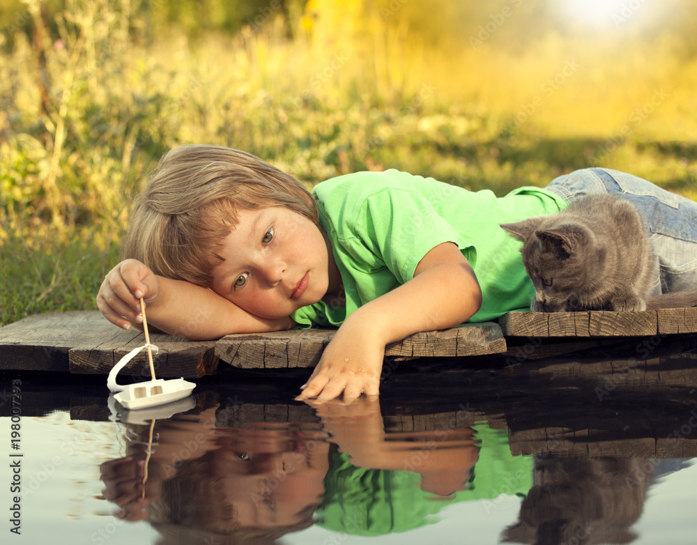 boy and his beloved kitten playing with a boat from pier in pond summer evening boy and his beloved kitten playing with a boat from pier in pond summer evening