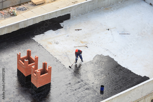 Two workers conduct waterproofing of the roof with bitumen. View from above. photo