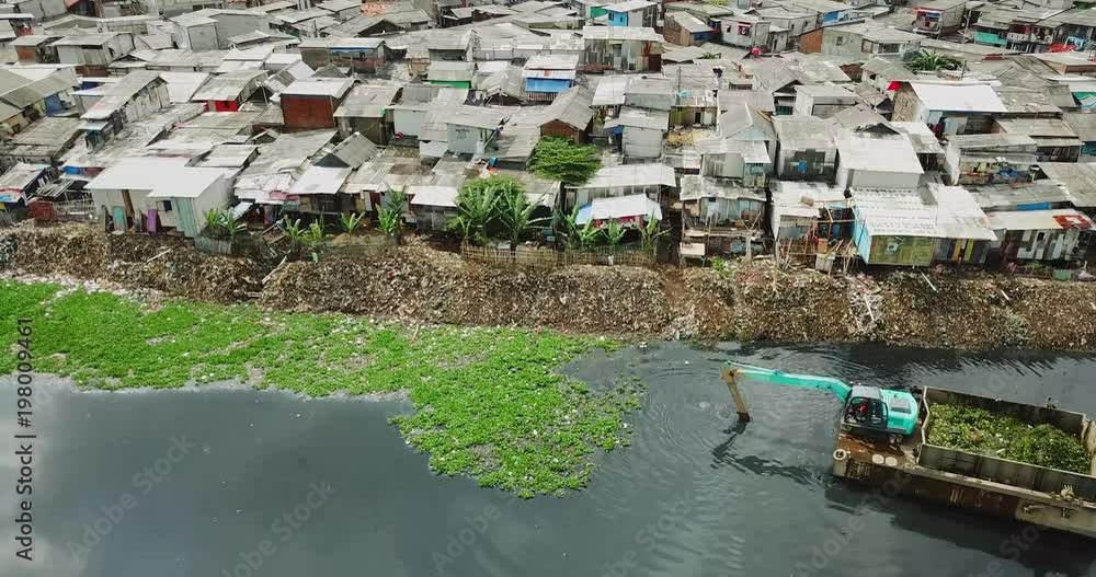 JAKARTA - Indonesia. March 20, 2018: Drone view of an excavator removing water plant and waste on the lakeside with slum houses background. Shot in 4k resolution JAKARTA - Indonesia. March 20, 2018: Drone view of an excavator removing water plant and waste on the lakeside with slum houses background. Shot in 4k resolution