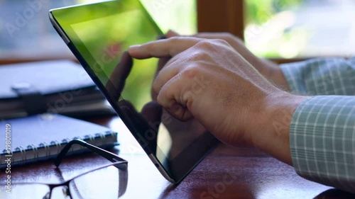 Man using tablet device at desk, backlit by sunshine with reflections through window, close up.