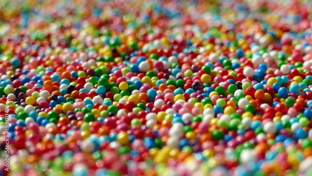 A multi-colored dragee spins on a plate. Multicolored balls. All the colors of the rainbow. Colored easter dragees. Red blue green yellow white white orange. A multi-colored dragee spins on a plate. Multicolored balls. All the colors of the rainbow. Colored easter dragees. Red blue green yellow white white orange.