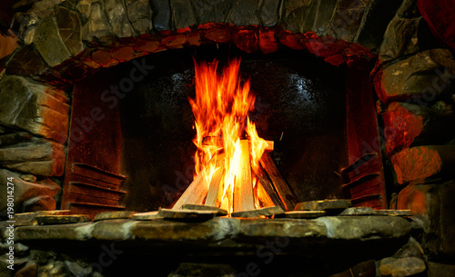 A burning tree in a brick home fireplace, a flame on a dark background.