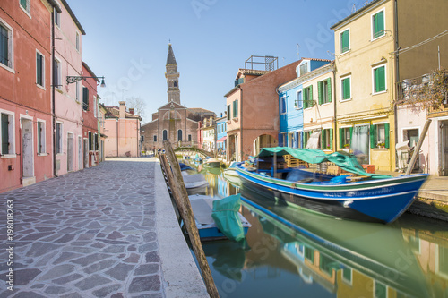 Typical canal with colorful facades with vibrant colors and Church of San Martino and its leaning campanile in famous fishermen village on the island of Burano, Venice, Italy