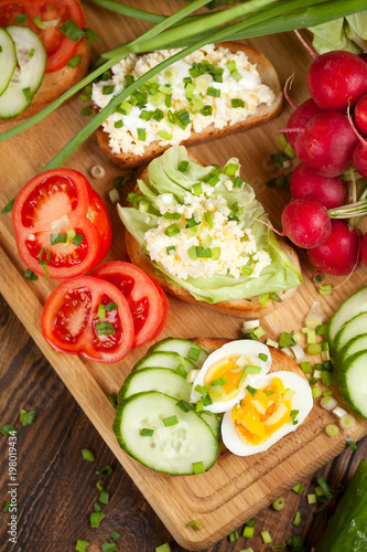 Summer sandwiches ingredients - cucumber, radish, tomato, mozzarella and eggs, white wood background, top view