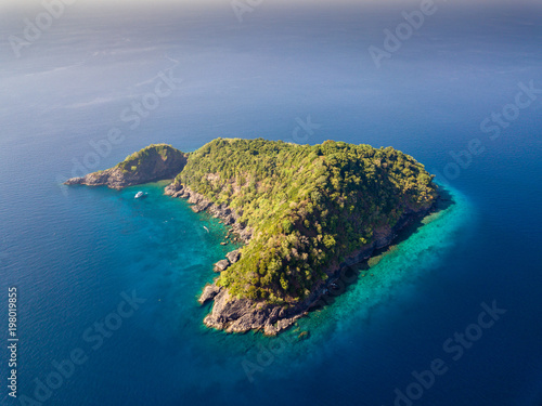 Aerial drone view of a tree covered tropical island surrounded by clear coral reef
