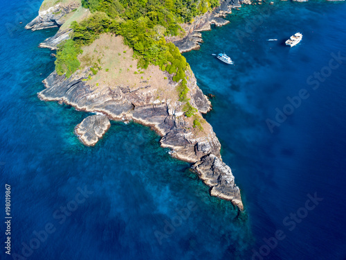 Aerial drone view of a tree covered tropical island surrounded by clear coral reef