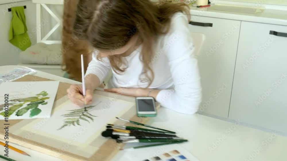 little beautiful red-haired woman paints with paint and brush sitting at table little beautiful red-haired woman paints with paint and brush sitting at table