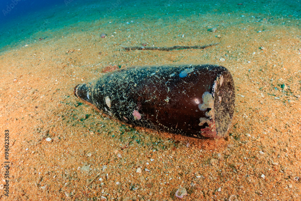 Underwater pollution - a discarded bottle litters the sea bed on a sandy bottom Underwater pollution - a discarded bottle litters the sea bed on a sandy bottom