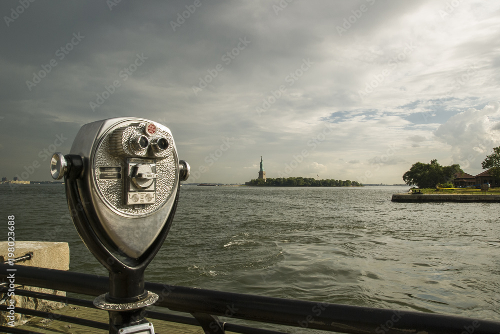 Tower viewer/Abstract image of a coin operated public telescope binoculars on the bay shore across from the Statue of Liberty and Ellis Island in New York City. Tower viewer/Abstract image of a coin operated public telescope binoculars on the bay shore across from the Statue of Liberty and Ellis Island in New York City.