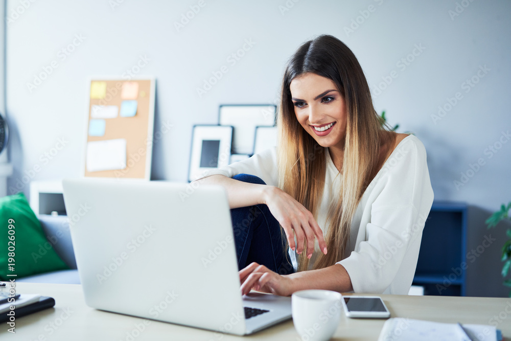 Beautifull young woman using laptop and drinking coffee while sitting at desk at home Beautifull young woman using laptop and drinking coffee while sitting at desk at home