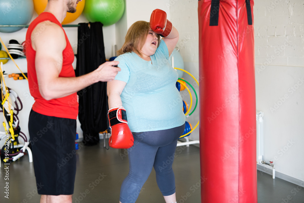 Portrait of exhausted obese woman wiping sweat from forehead during boxing training in gym