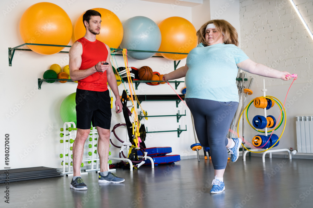 Full length portrait of overweight woman jumping with rope in during