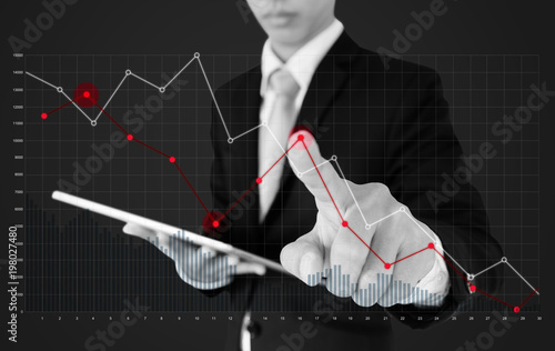 Businessman using digital tablet and pointing finger on falling graph diagram. Business finance and economy crisis photo