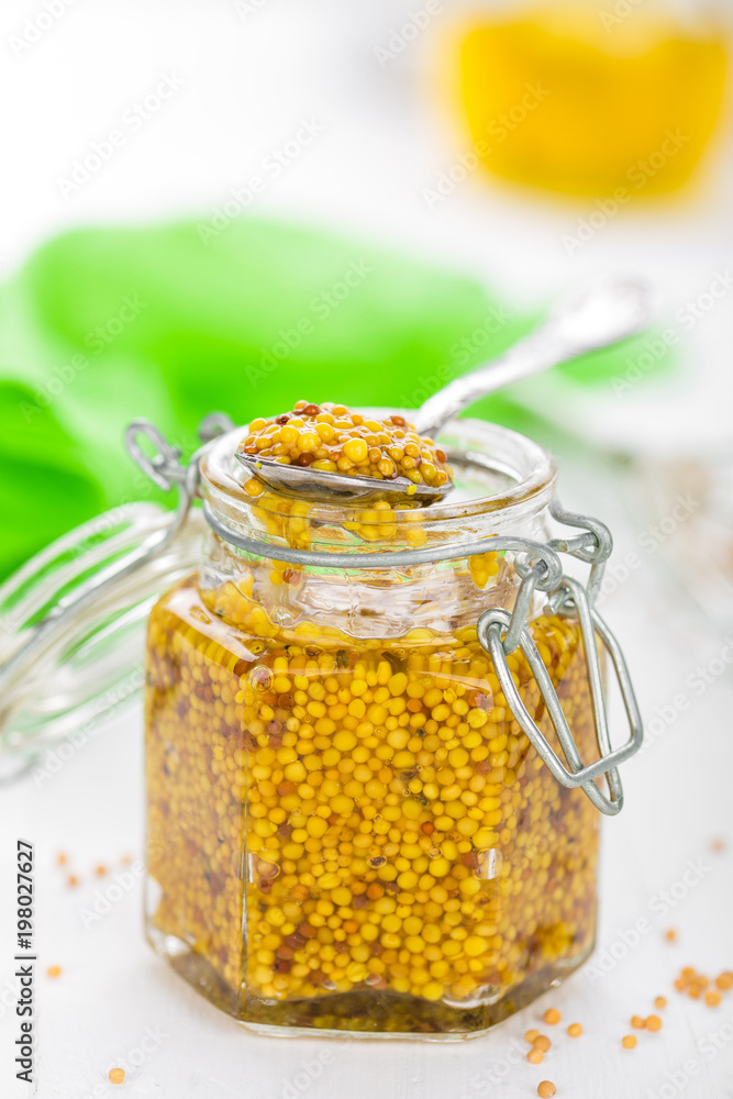 Mustard in glass jar on white wooden table closeup. Dijon mustard Mustard in glass jar on white wooden table closeup. Dijon mustard