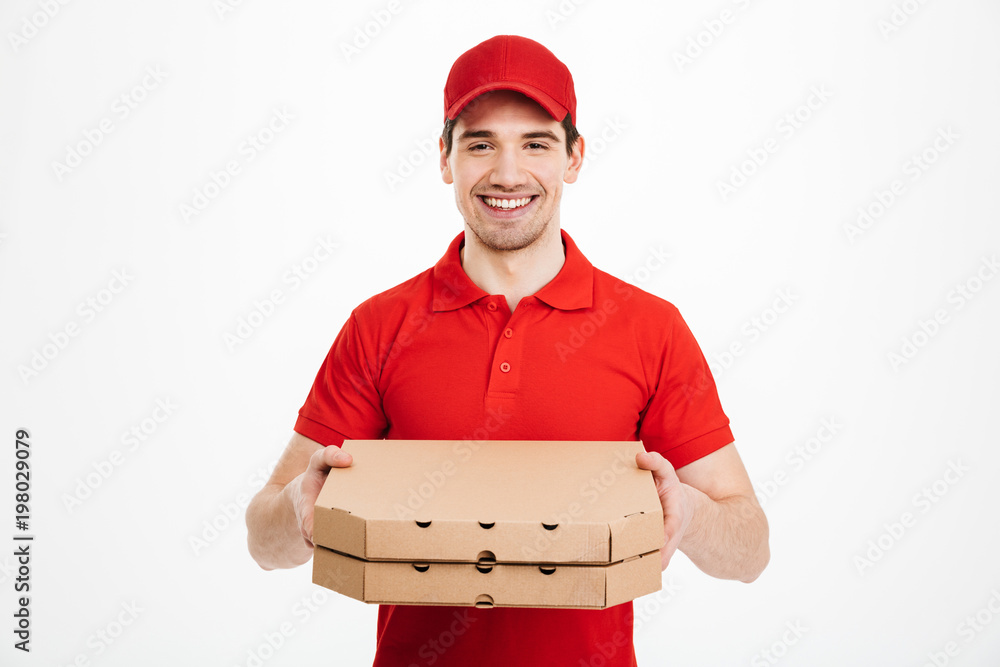 Photo of happy man from delivery service in red t-shirt and cap giving food order and holding two pizza boxes, isolated over white background Photo of happy man from delivery service in red t-shirt and cap giving food order and holding two pizza boxes, isolated over white background