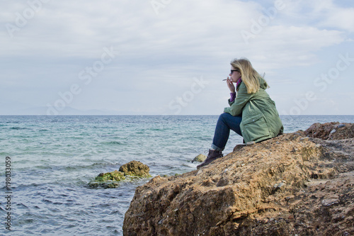 Young blonde girl Smoking on a rocky shore alone and looking away