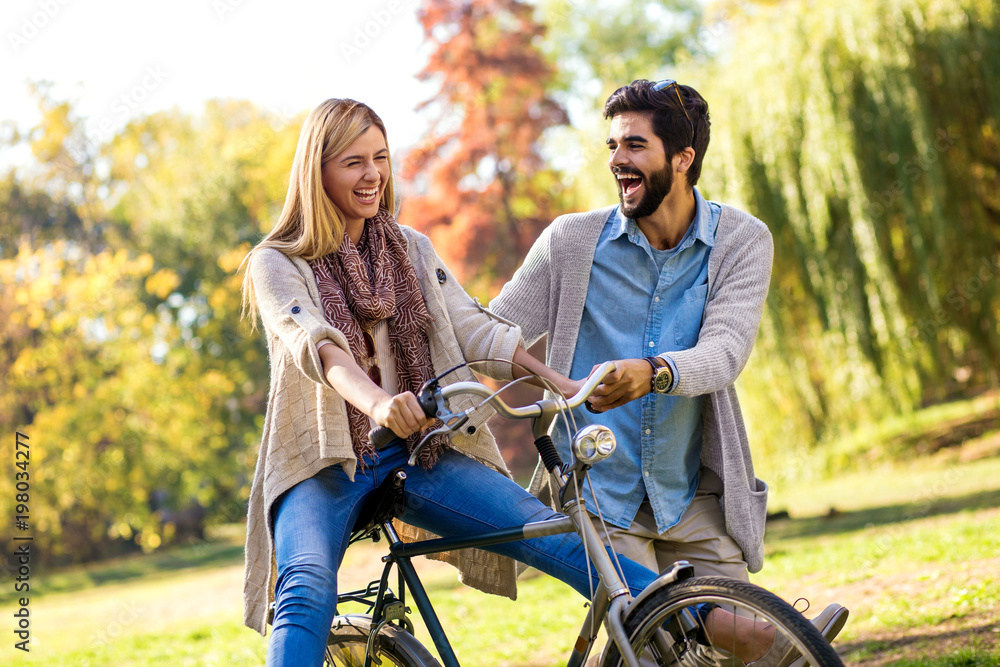 Obraz premium Happy young couple having fun riding a bicycle on sunny day in the park. 
