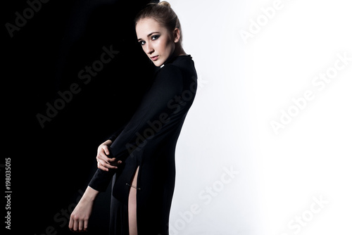 Young female model in black dress on the contrast black and white background. Fashion art studio photo