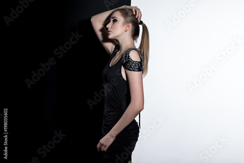 Young female model in black dress on the contrast black and white background. Fashion art studio photo