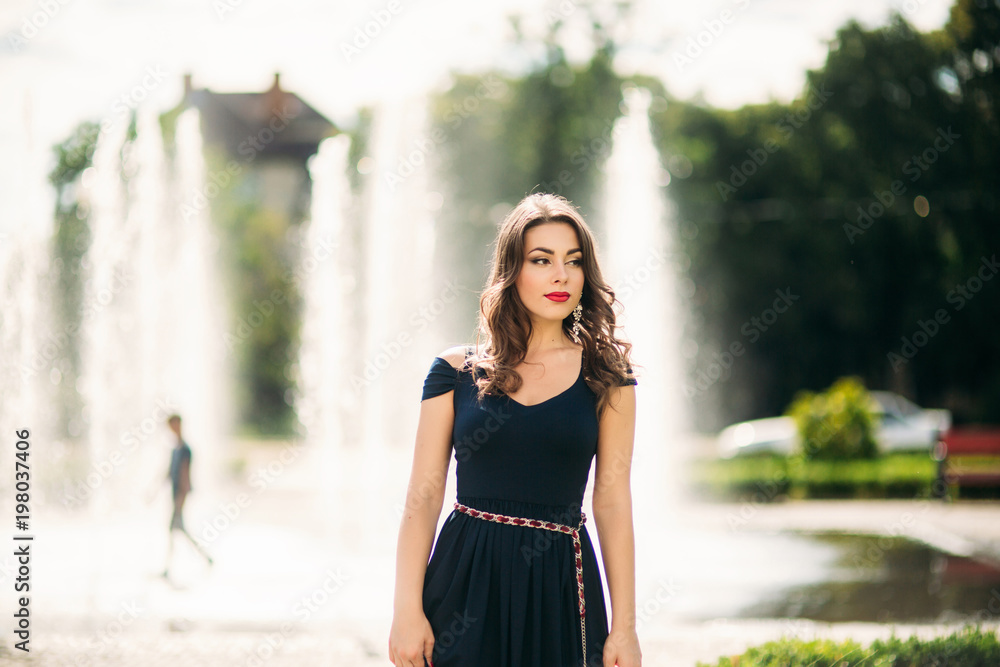 A girl is walking around the city, near a large fountain.