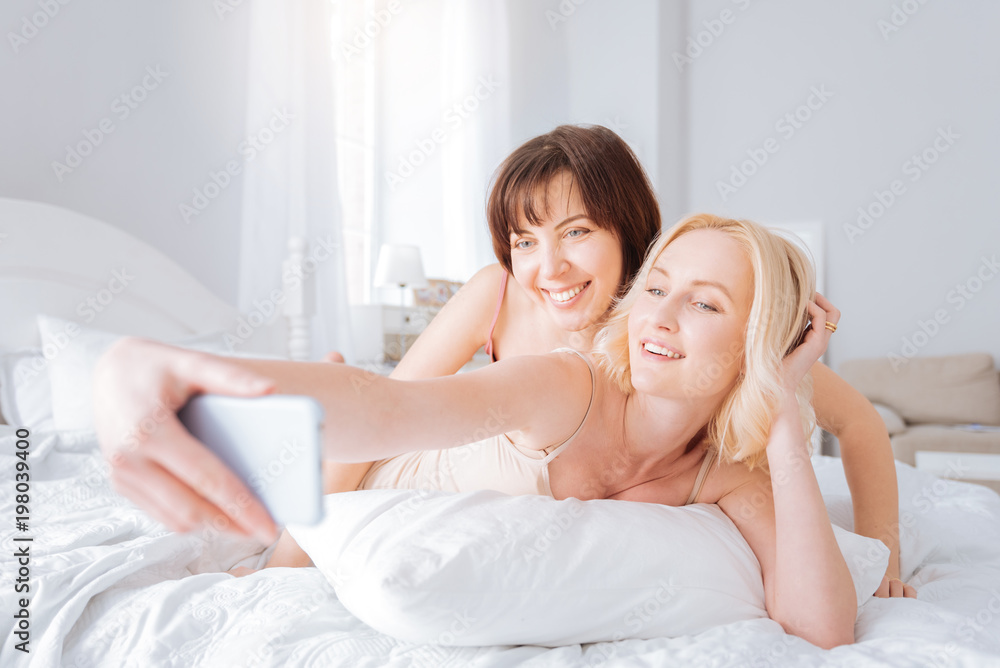 Moments to remember. Nice cheerful delighted woman lying on the bed and smiling while taking a selfie Moments to remember. Nice cheerful delighted woman lying on the bed and smiling while taking a selfie