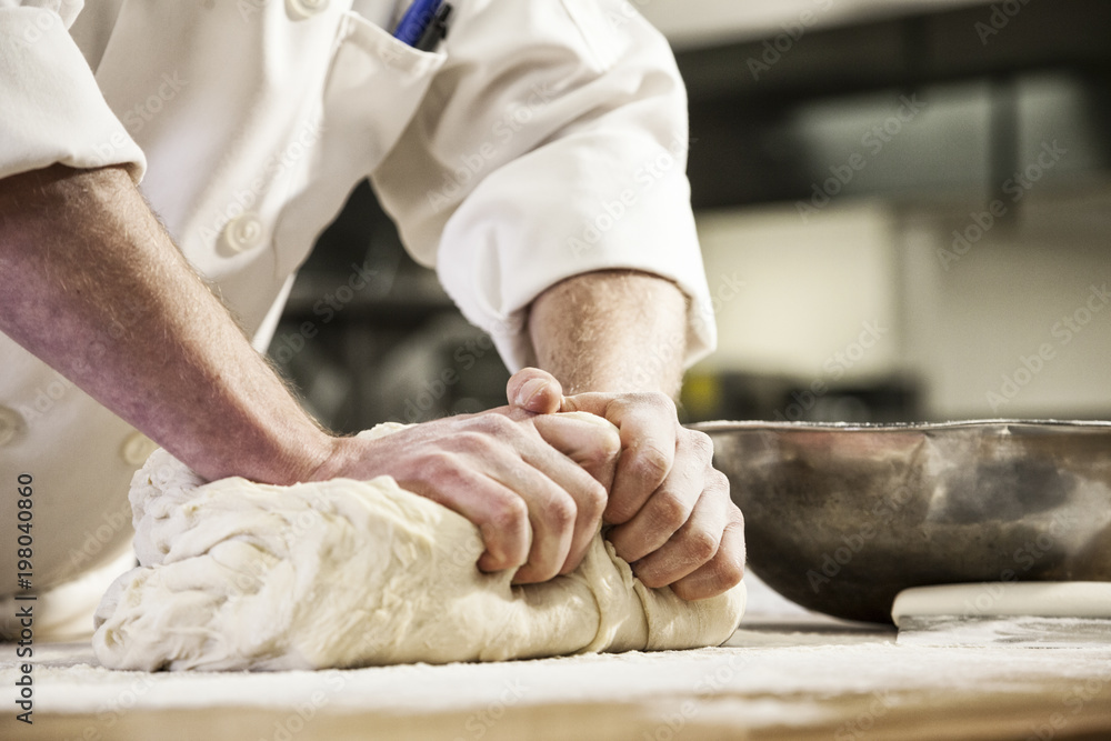 A chef's hands kneading bread dough on a floured worktop. foto de Stock Adobe Stock