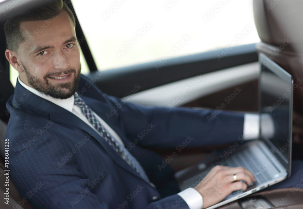 Confident businessman with laptop sitting in auto.
