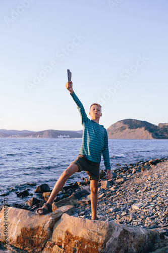 Foto boy standing on the sea shore with a stick in his hands in a heroic pose