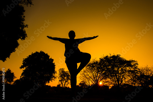 Silhouette chuuby man doing yoga over sunrise in the morning.