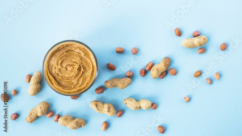 A jar of hazelnut paste among peanuts in shell and without on a blue background. Vegan product. American breakfast. Top view, Flat lay