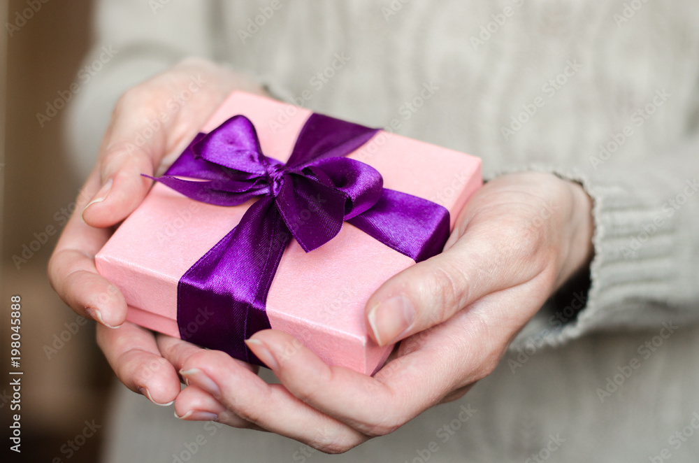 Young woman holds a gift box with a bow close up Young woman holds a gift box with a bow close up