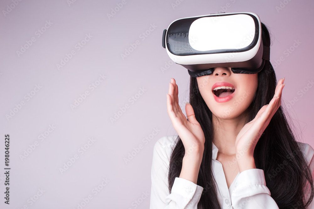 Studio Portrait of young beautiful smiling surprised Asian girl  in white shirt watching video in virtual reality headset glasses. Free copy space provided. New technologies concept