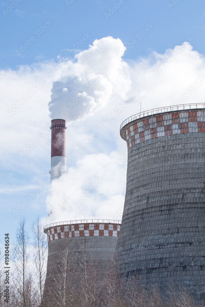 The steaming pipe and cooling towers of the winter thermal power station on the background of the blue sky.