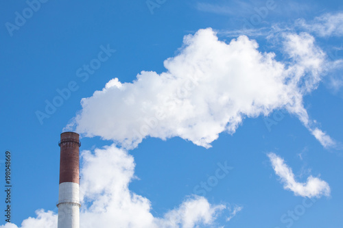 The steaming pipe of the plant or factory on the background of the blue sky.