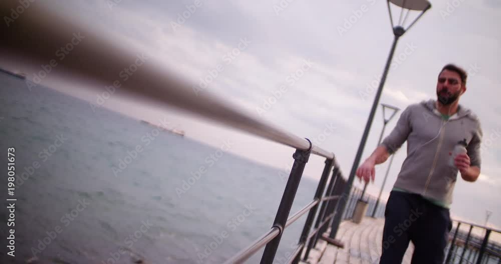 Young fit man running on pier holding a water bottle