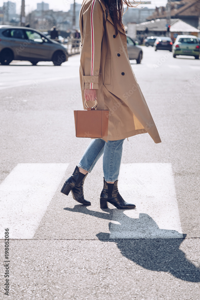 street style portrait of an attractive woman wearing a beige trench coat,  denim jeans, ankle boots,