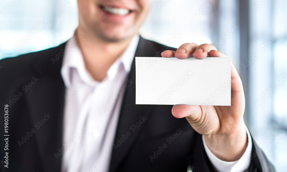Happy smiling business man holding empty white business card in modern office building. Free blank copy space. Happy smiling business man holding empty white business card in modern office building. Free blank copy space.