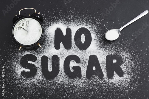 Obraz na płótnie Spoonful of sugar and an alarm clock, covered with sugar on a dark table, sugar written the text